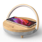 The Clérachic 3-in-1 lamp in wood finish, a phone charging on the pad below the lit arch.