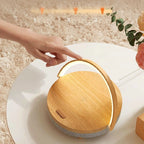 A hand touching the Clérachic lamp's wooden top to step through its three brightness levels.