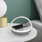 The Clérachic 3-in-1 lamp lit on a bedside table against a green wall, phone charging on top.