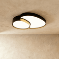 Clérachic matte black overlapping-disc ceiling light, lit warm white, mounted flush against a plastered living room ceiling.
