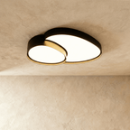 Clérachic matte black overlapping-disc ceiling light, lit warm white, mounted flush against a plastered living room ceiling.