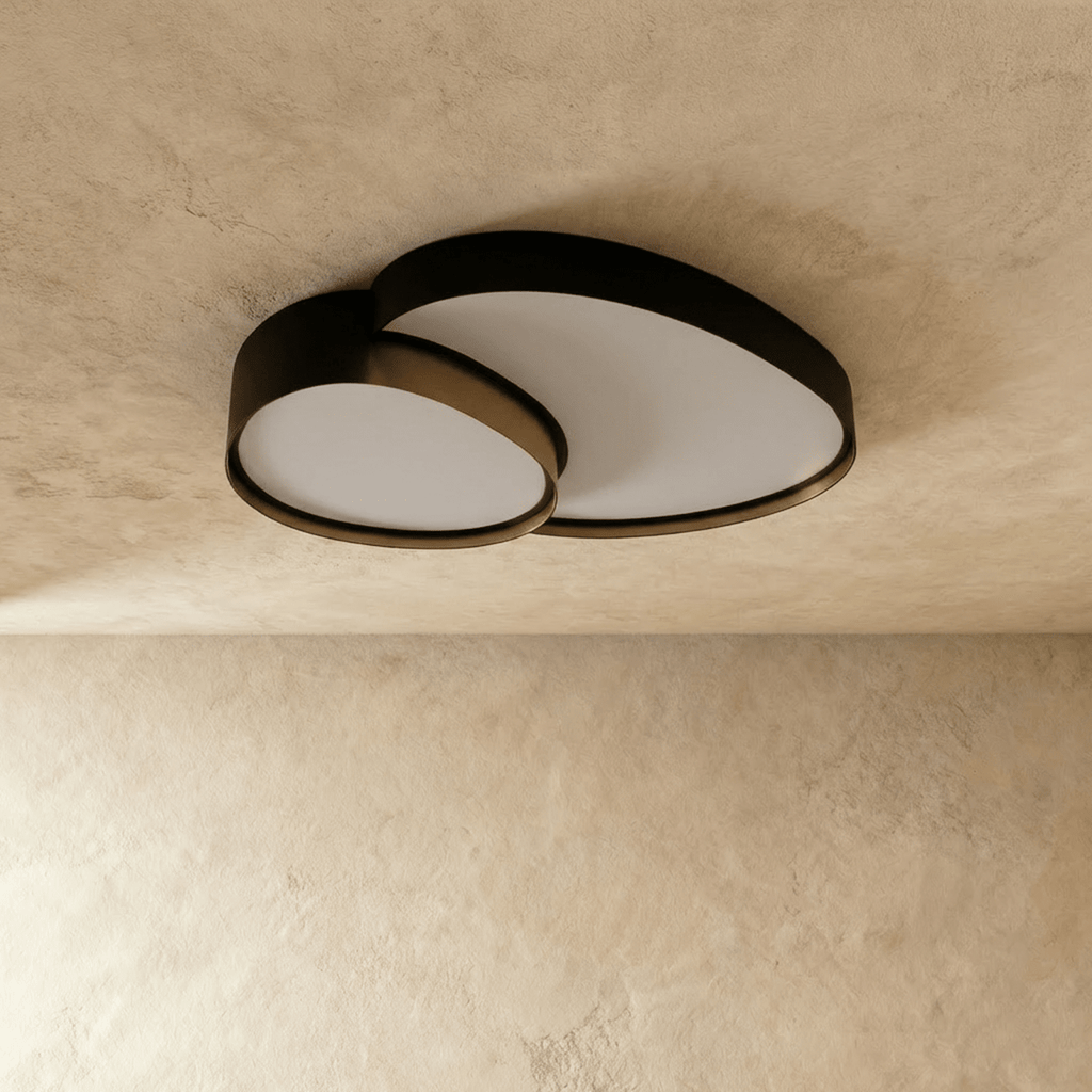 A slightly angled view of the Clérachic black overlapping-disc ceiling light, its acrylic panels glowing warm white overhead.