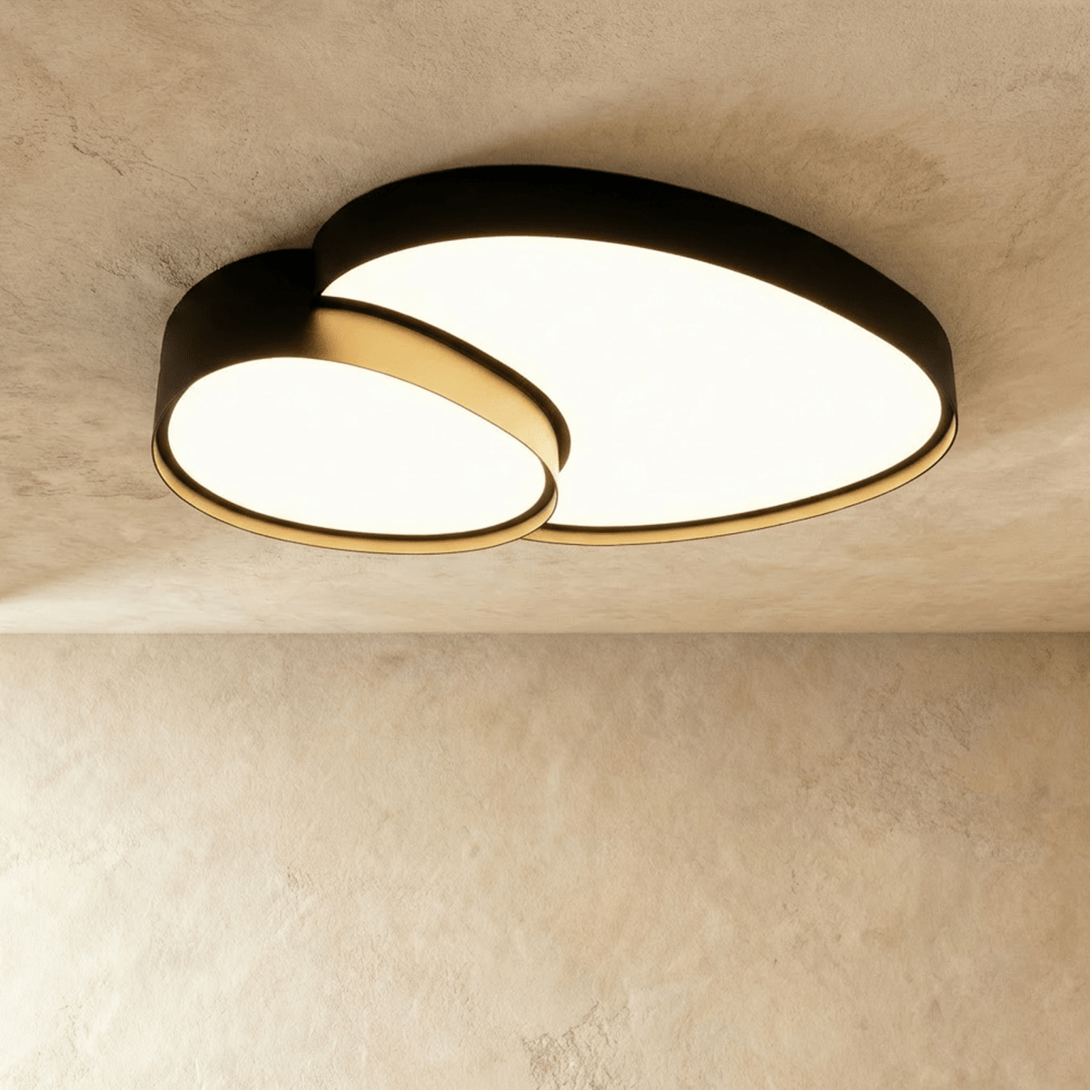 Another angle of the Clérachic matte black ceiling light, its two overlapping discs glowing warm white above a plastered wall.