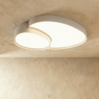 Side angle of the Clérachic white overlapping-disc ceiling light, its acrylic panels lit warm white in a minimalist room.