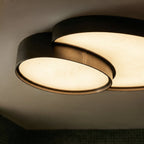 Close-up of the Clérachic black ceiling light's overlapping acrylic discs and brushed metal joint, glowing warm white.