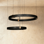 Clérachic ring chandelier in two tiers, black perforated rings joined by brass mounts against a textured wall.