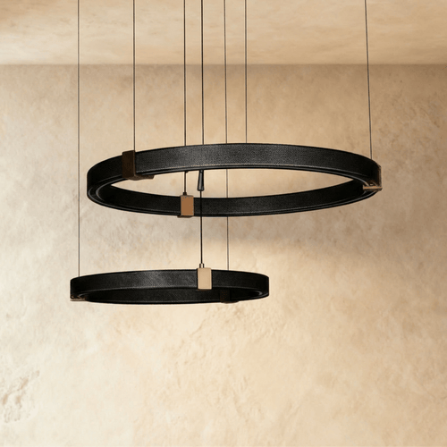 Clérachic ring chandelier in two tiers, black perforated rings joined by brass mounts against a textured wall.