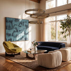 Clérachic three-tier ring chandelier lit warm in a living room, hung above a navy sofa and glass coffee table.