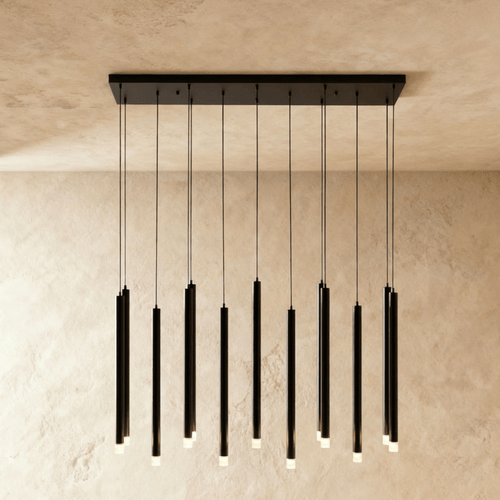 Clérachic black linear chandelier of slender cylinders with frosted lit tips, hung from a black rectangular canopy on a limewash wall.