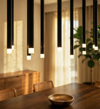 Clérachic close-up of black chandelier tubes with glowing frosted acrylic ends above a walnut table, wooden bowl and sideboard.