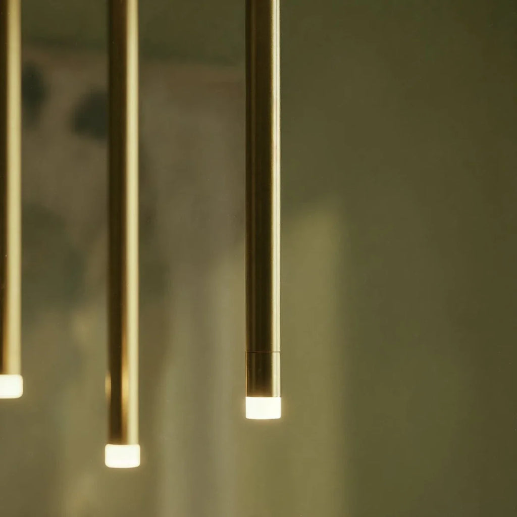 Clérachic close-up of three gold aluminium tubes, each ending in a softly glowing frosted acrylic diffuser, on an olive background.
