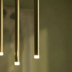 Clérachic close-up of three gold aluminium tubes, each ending in a softly glowing frosted acrylic diffuser, on an olive background.