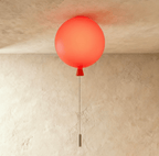 Clérachic balloon-shaped ceiling light glowing coral red, with a red cone neck and a thin pull cord, against a textured plaster wall.