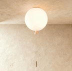 Clérachic opal white balloon ceiling light glowing warmly, with a white cone neck and pull cord, set against limewashed plaster.