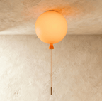 Clérachic balloon-shaped ceiling light glowing soft orange, with an orange cone neck and cord, fixed to a plaster ceiling.