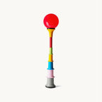 Red glass globe on a stacked column of multicolour tiers, this Clérachic floor lamp on a plain off-white backdrop.