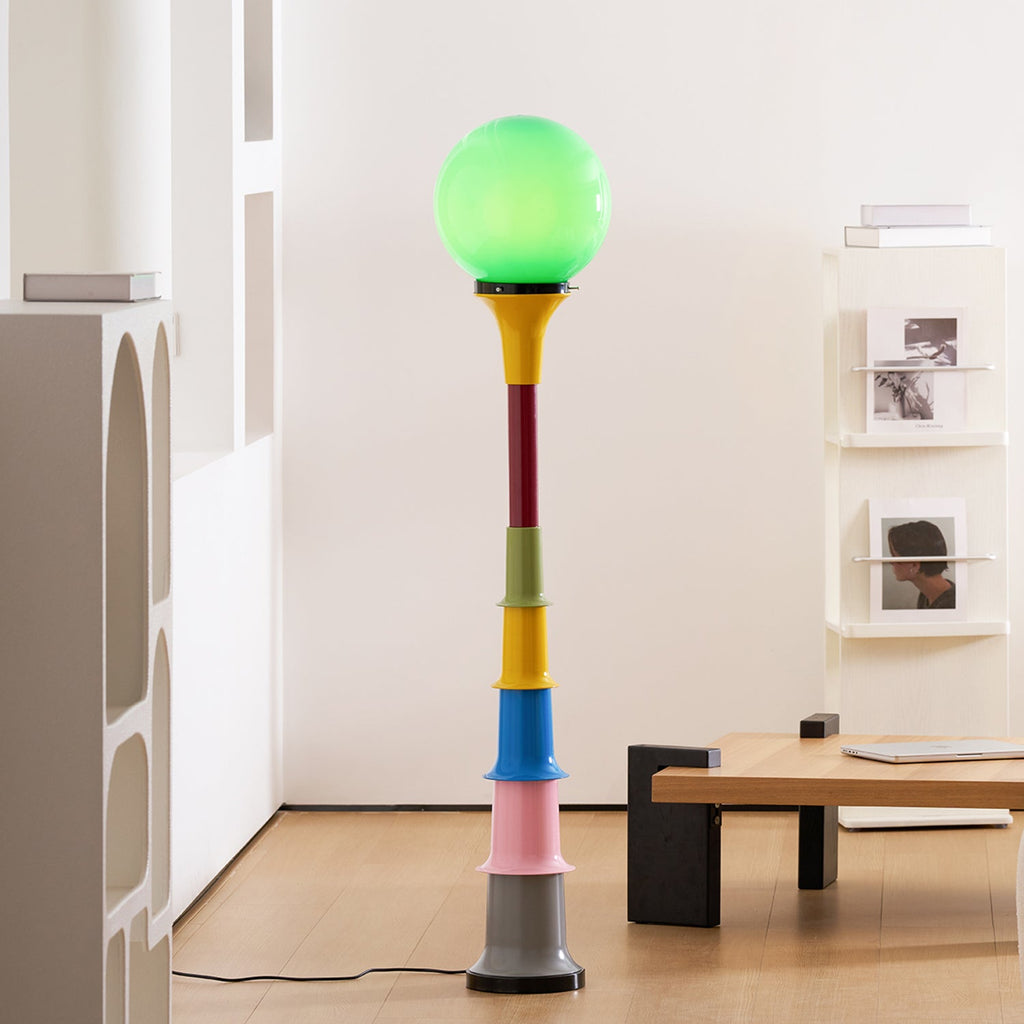 A Clérachic floor lamp with a green globe and a multicolour stacked stem, in a bright room with a low wooden table.