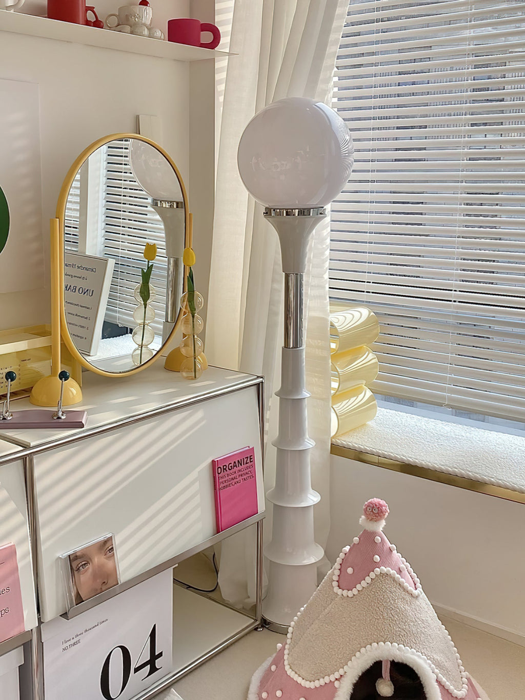 White-globe Clérachic floor lamp with a cream ribbed stem, beside a vanity mirror and a dressing table in a bright room.