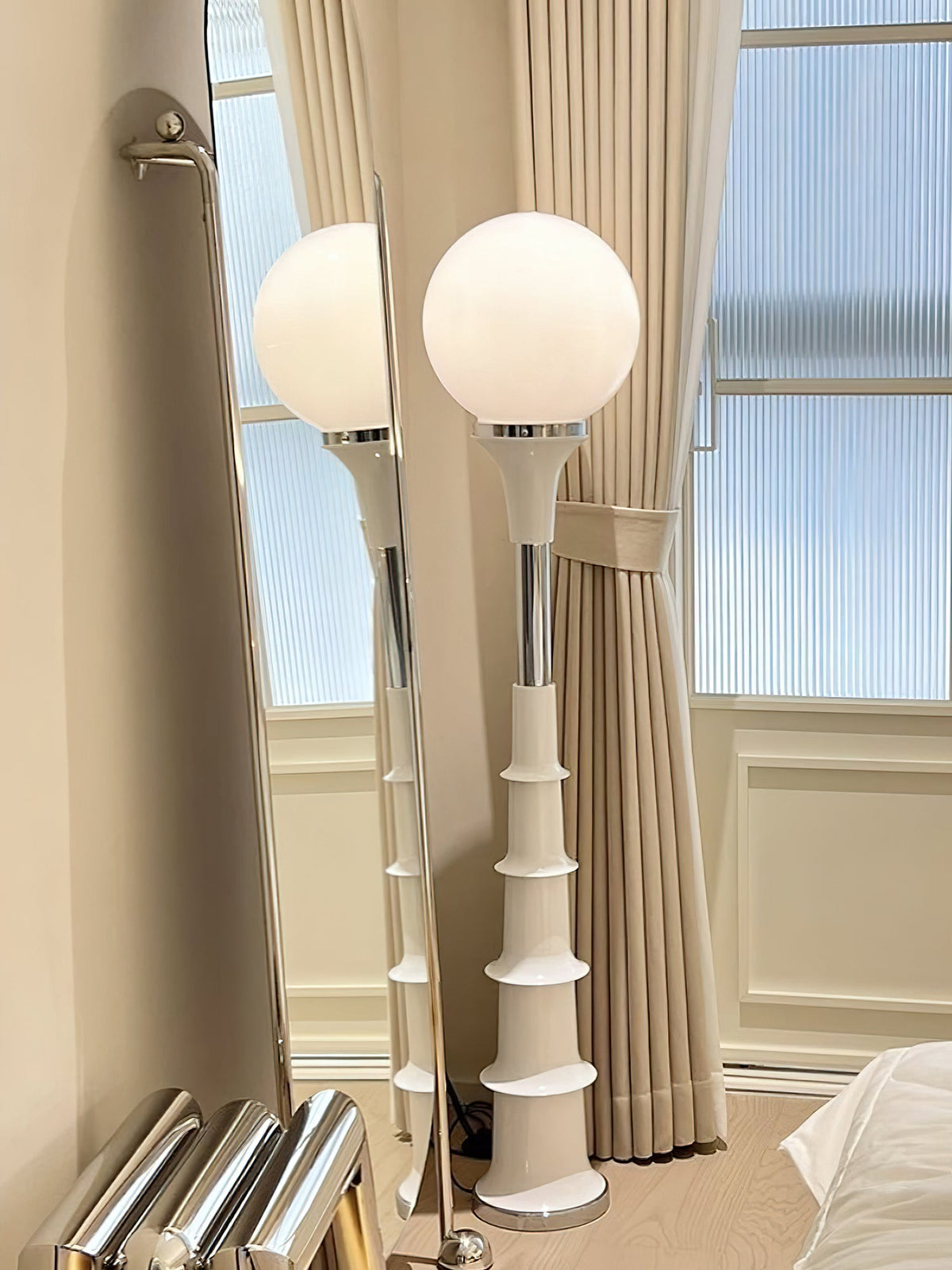 Two white-globe Clérachic floor lamps standing beside tall curtains in front of a window with ribbed glass.