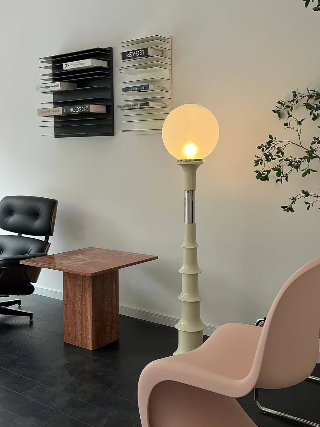 Clérachic floor lamp with a softly lit globe and a pale ribbed stem, beside a dark leather chair and a pink moulded chair.