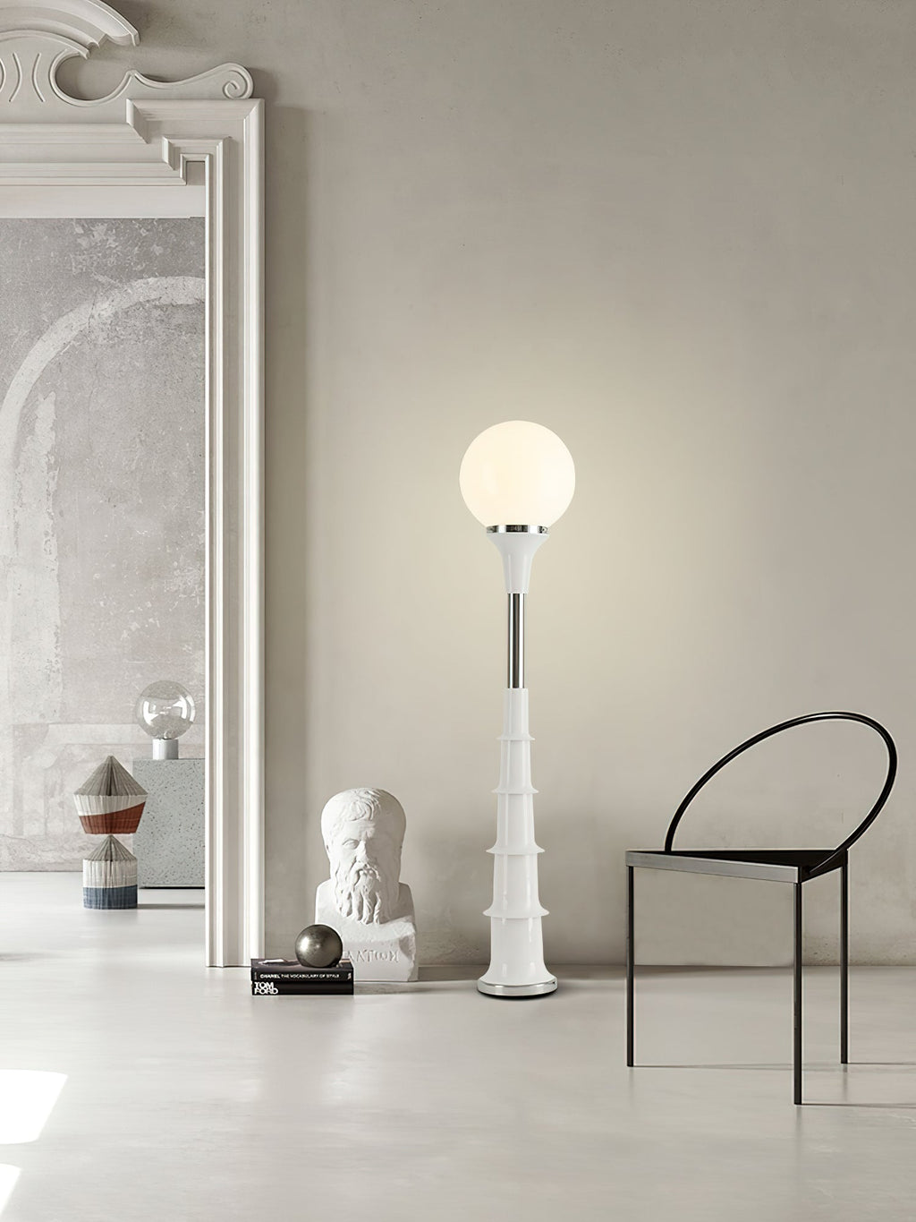 White-globe Clérachic floor lamp on a pale ribbed stem, standing in a large grey room with a black chair and a plaster bust.