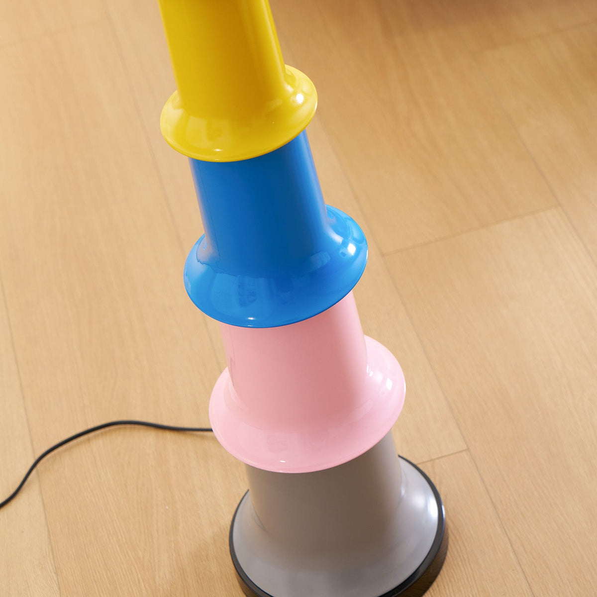 Close view of the yellow, blue and pink tiers and grey foot of this Clérachic floor lamp on a wooden floor.