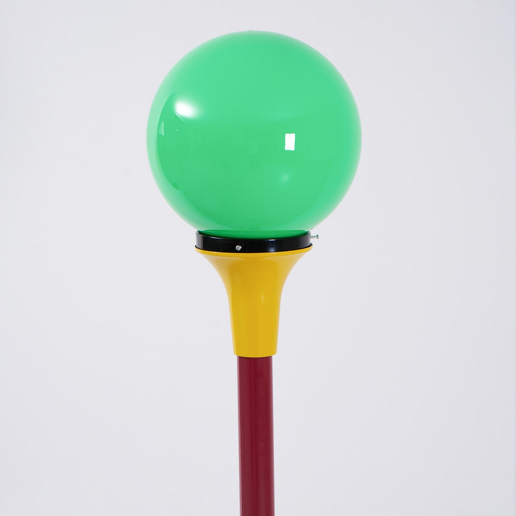 Close view of a green glass globe sitting on a yellow funnel above a deep red stem on this Clérachic floor lamp.