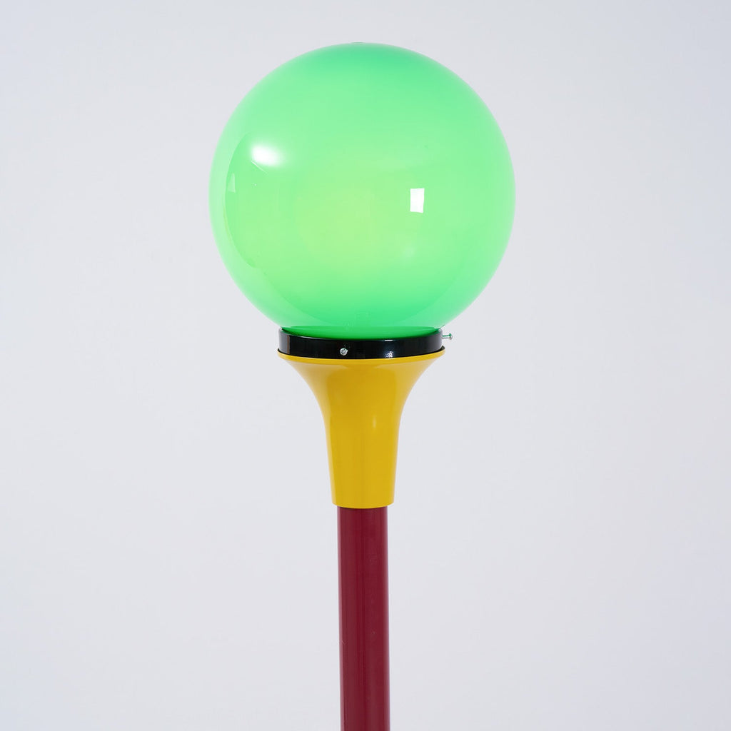 Close view of the lit green globe and yellow funnel on this Clérachic floor lamp, with the red stem below.