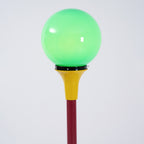 Close view of the lit green globe and yellow funnel on this Clérachic floor lamp, with the red stem below.