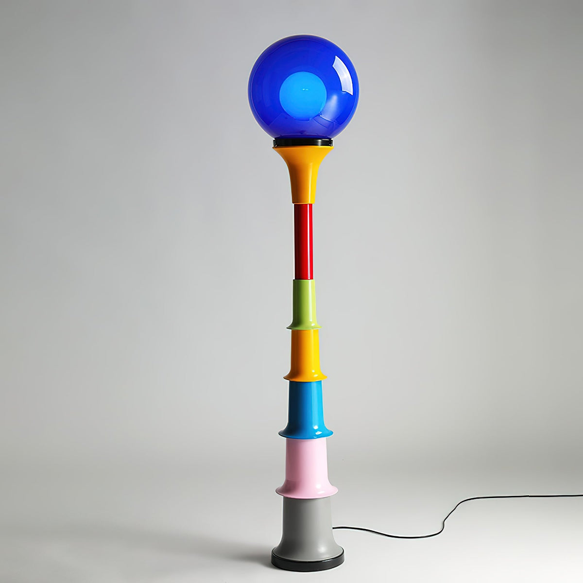 Blue-globe Clérachic floor lamp with a yellow funnel and multicolour tiers on a grey studio backdrop.
