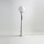 Clérachic floor lamp with a white globe and a pale ribbed stem with a chrome band, on a grey studio backdrop.