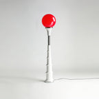 Red-globe Clérachic floor lamp with a white ribbed stem and chrome band, against a pale grey studio backdrop.
