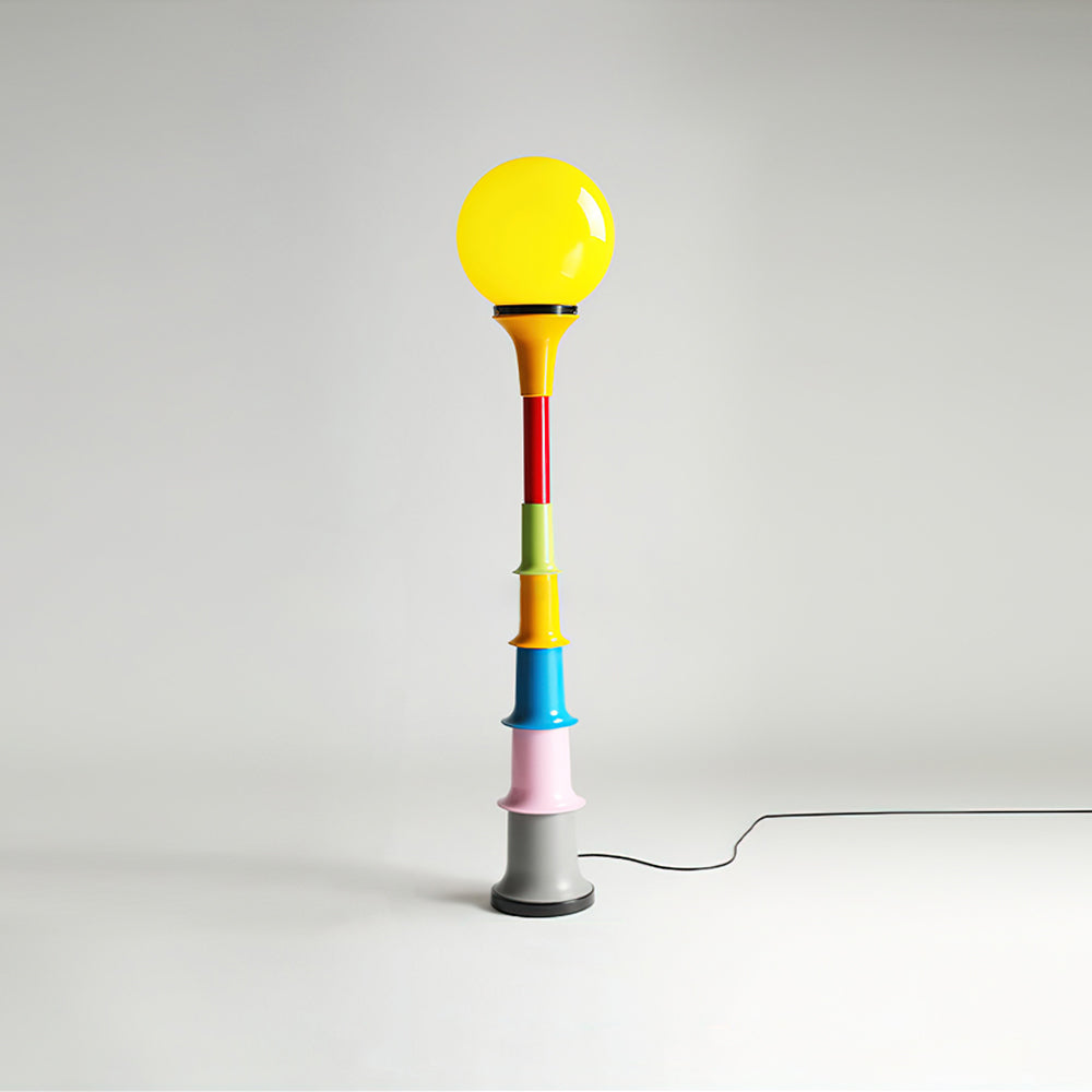 A Clérachic floor lamp with a yellow globe and a multicolour stacked stem, on a grey studio backdrop.