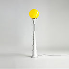Yellow-globe Clérachic floor lamp with a white ribbed stem and a chrome band, on a plain grey backdrop.