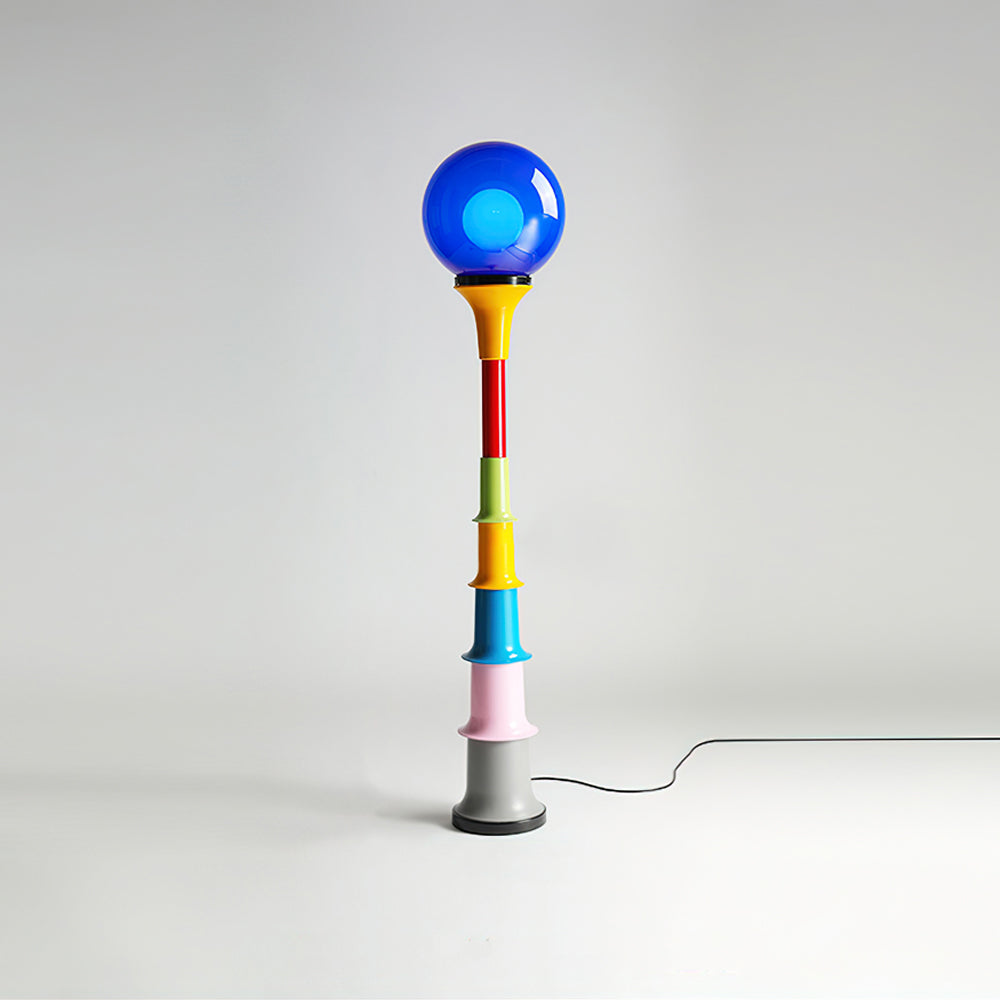 Clérachic floor lamp with a blue globe and a multicolour stacked stem, with its cord looping across the studio floor.