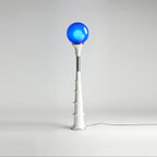 Blue-globe Clérachic floor lamp with a white ribbed stem and a chrome band, on a pale grey backdrop.
