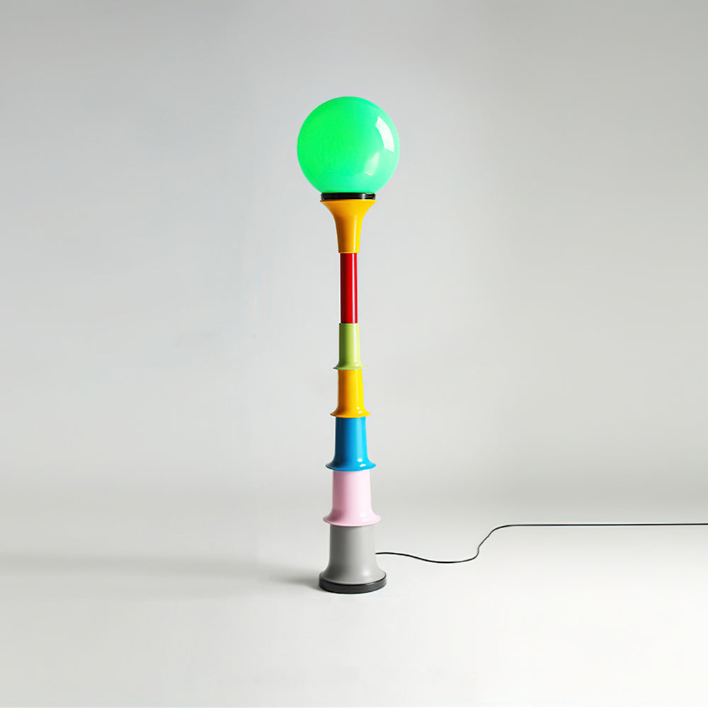 Clérachic floor lamp with a lit green globe and a stack of coloured tiers over a grey foot, on a light backdrop.