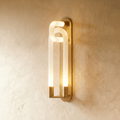 Clérachic wall light of interlocking frosted loops on a slim brass backplate, glowing warm against a limewashed wall.