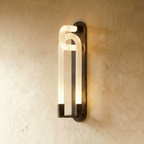 Clérachic wall light in a dark bronze finish, its interlocking frosted loops lit warm against a limewashed wall.