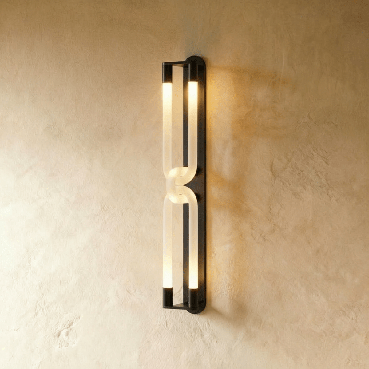 Clérachic tall wall light with two linked frosted loops and dark metal end caps, lit on a textured plaster wall.