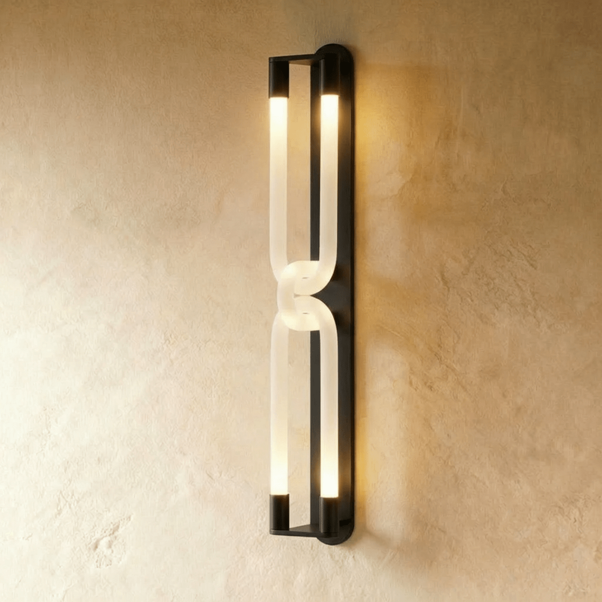 Clérachic tall wall light in dark metal, two interlocked frosted loops glowing at both ends on a plaster wall.