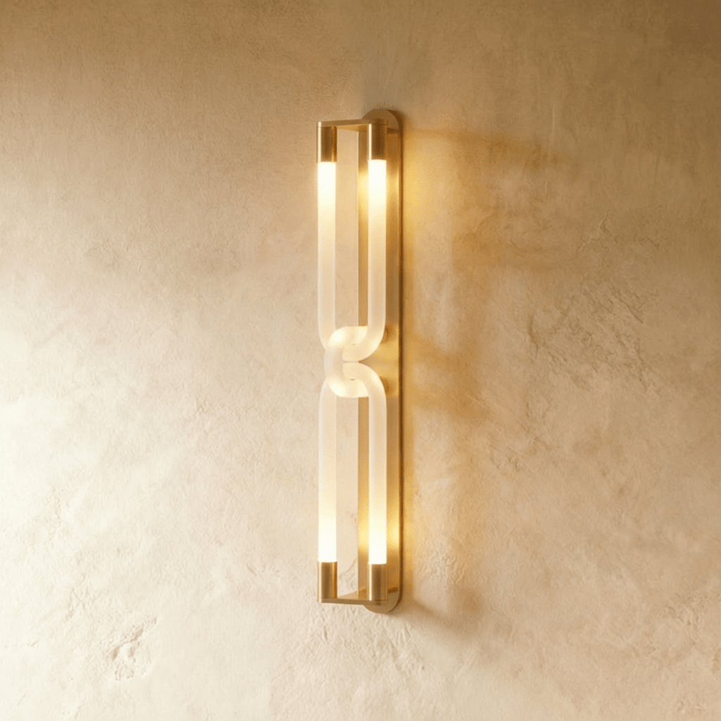 Clérachic tall wall light with brushed gold end caps and linked frosted loops glowing on a limewashed wall.