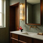 Clérachic brass wall light with frosted loops beside a walnut door frame and green mosaic tiles, above a stone vanity.