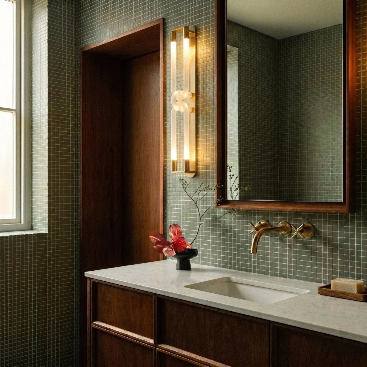 Clérachic brass wall light with frosted loops beside a walnut door frame and green mosaic tiles, above a stone vanity.
