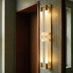 Clérachic gold wall light with interlocked frosted loops, close beside a walnut door frame on green mosaic tiles.