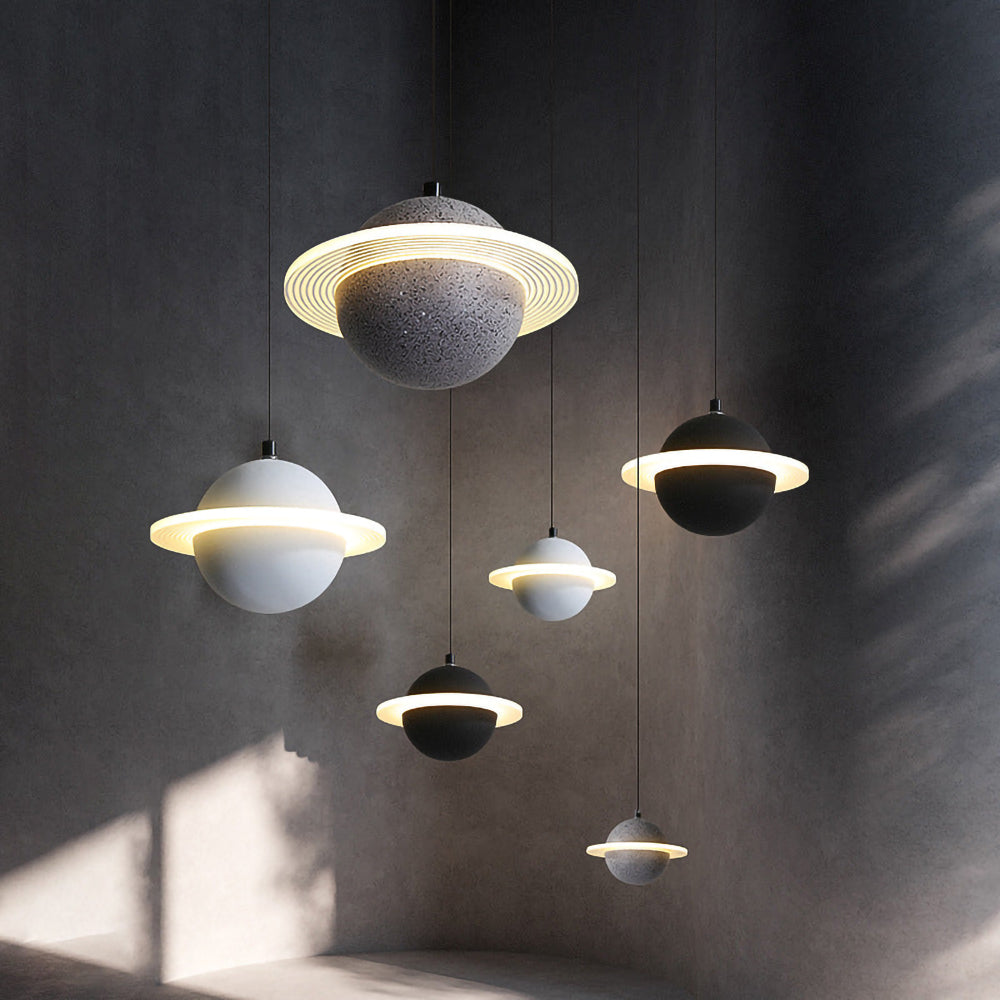 Five Clérachic planet pendants in grey and black hang at different heights against a dark textured wall, each with a glowing ring.