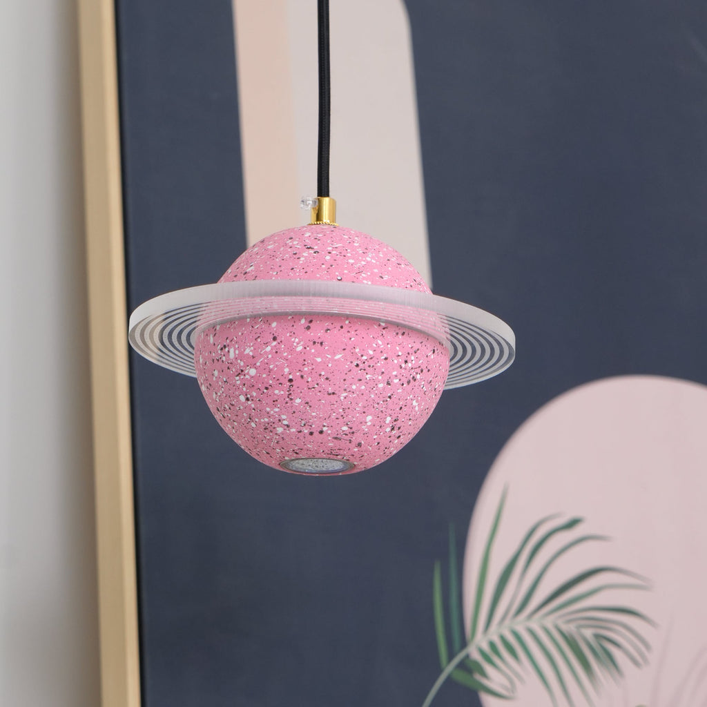 Unlit sand pink Clérachic pendant with a frosted ring hanging in front of a gold-framed navy and pink print with palm leaves.