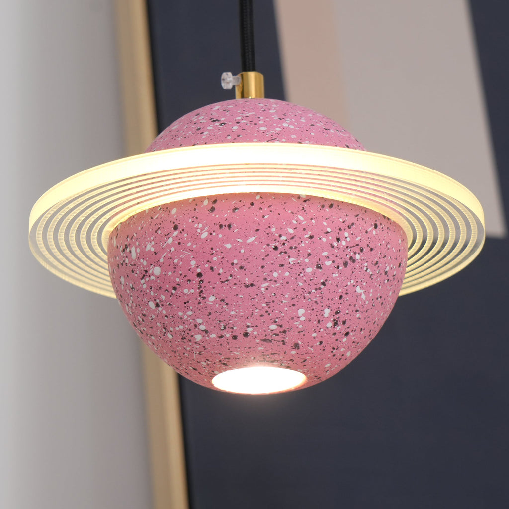 Close view of the sand pink Clérachic pendant, with its ridged glowing ring, brass cord top and a bright bulb under the sphere.
