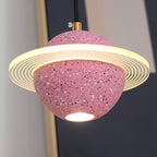 Close view of the sand pink Clérachic pendant, with its ridged glowing ring, brass cord top and a bright bulb under the sphere.