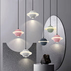 Group of Clérachic planet pendants in pink, white, green, black and grey, hanging at varied heights beside an oval mirror and a dark rock.